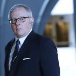 A man in a suit walks through an out-of-focus office building.