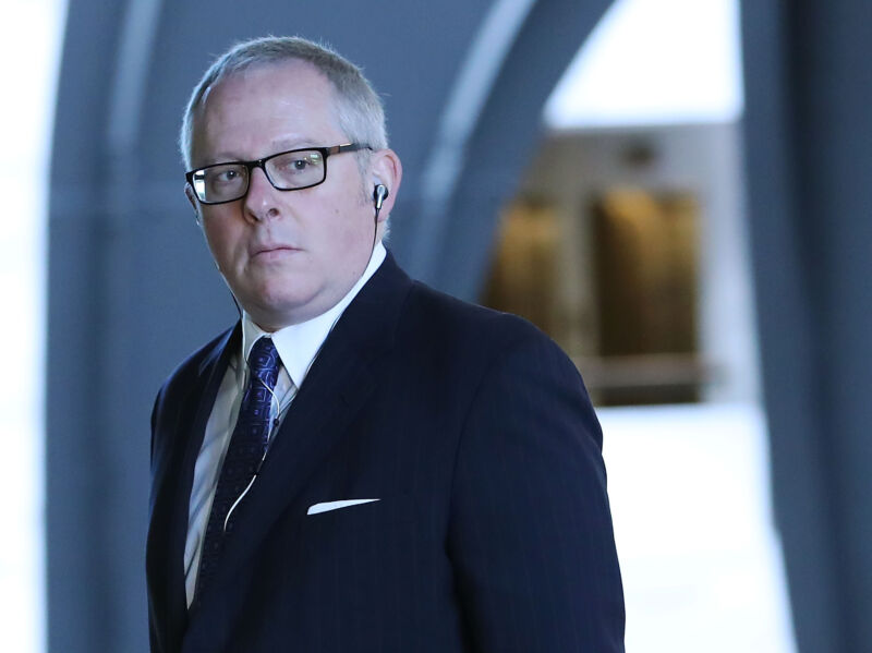 A man in a suit walks through an out-of-focus office building.