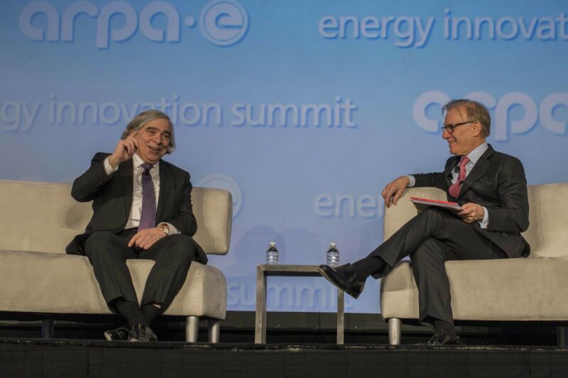 Two seated men in suits have a discussion on a stage.