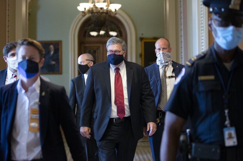 Attorney General William Barr walking down a hallway while wearing a mask.