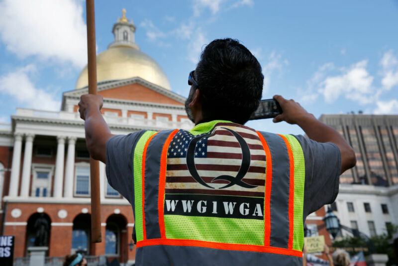 BOSTON—A man wearing a QAnon vest held a flag during a No Mandatory Flu Shot Massachusetts rally held outside of the State House in Boston on Aug. 30, 2020, to demonstrate against Gov. Charlie Baker