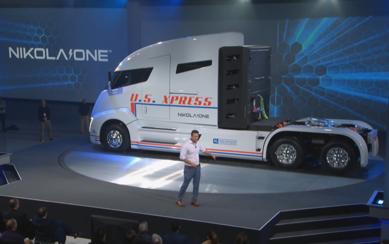 A man dressed casually holds a presentation in front of a semitruck.