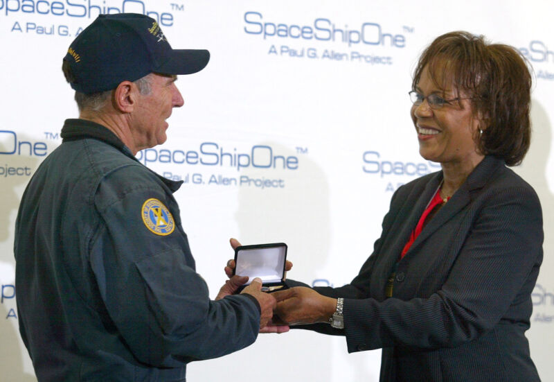 A woman excepts an award from a man in factory-style work clothes.