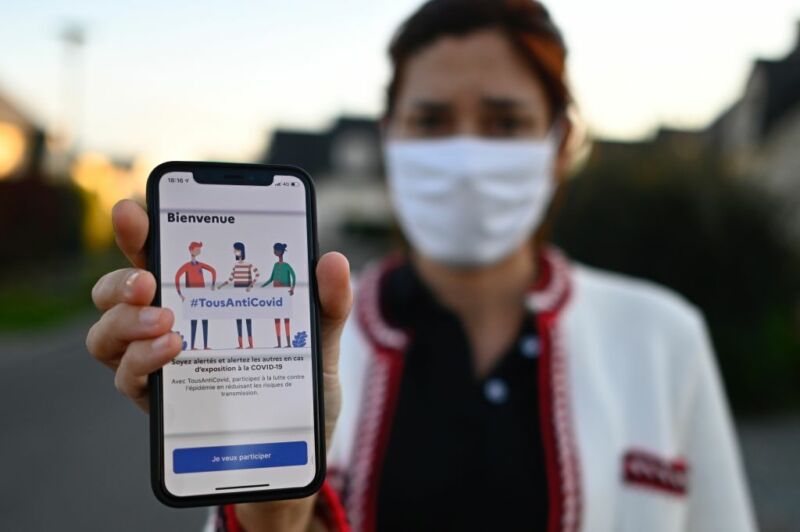 A woman in a face mask holds up a phone.