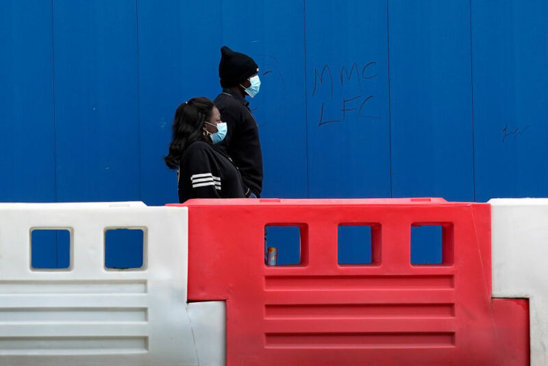 A masked man and woman walks outside a plastic barrier.