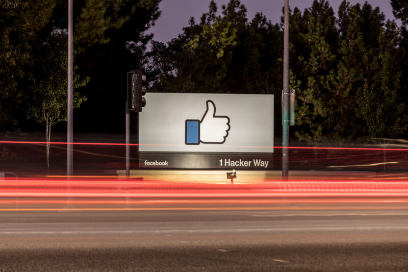 Facebook logo on a street sign outside a wooded campus.