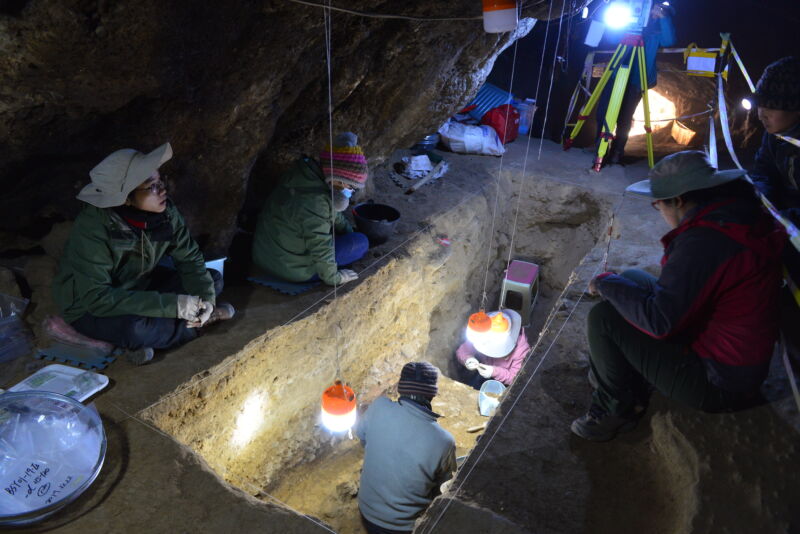 Image of a large, lit trench with people working in it.