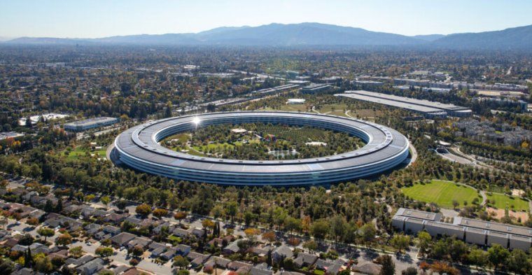 Un enorme edificio en forma de anillo en un campus verde.