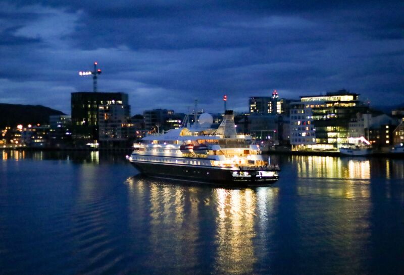 A relatively small luxury liner sails past a city at night.