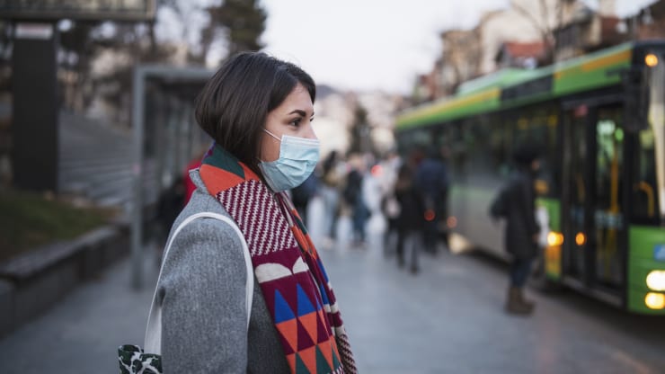 A woman wearing a medical mask and waiting for a bus