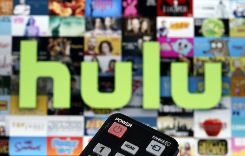 Photo illustration of a remote control in front of a television screen displaying Hulu TV content.
