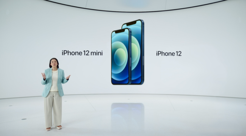 A woman gives a presentation in front of a giant video projector displaying two smartphones.