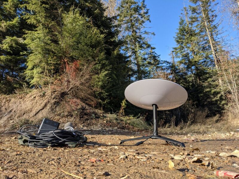 Una antena parabólica en un bosque junto a una fuente de alimentación portátil.