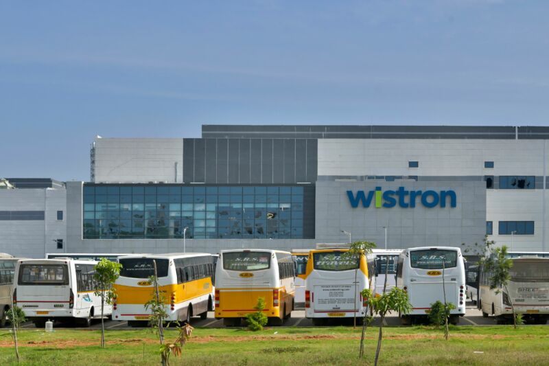 Buses surround a wide building of glass and steel.