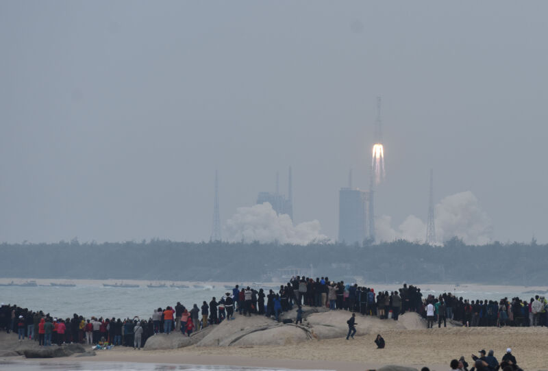 A body of water separates crowds from a rocket launch.