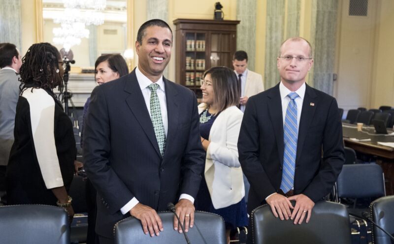 Federal Communications Commission Chairman Ajit Pai and FCC Commissioner Brendan Carr stand next to each other in a Senate hearing room.