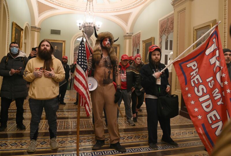 Men with flags and bizarre costumes pose for a photo in a neoclassical corridor.