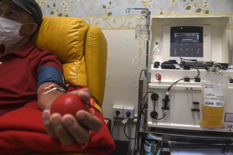 A man in a red shirt seated in a chair, donating blood.