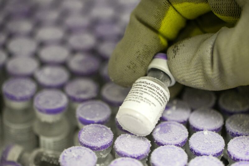 Extreme close-up photograph of gloved hand holding frost-covered glass vial.