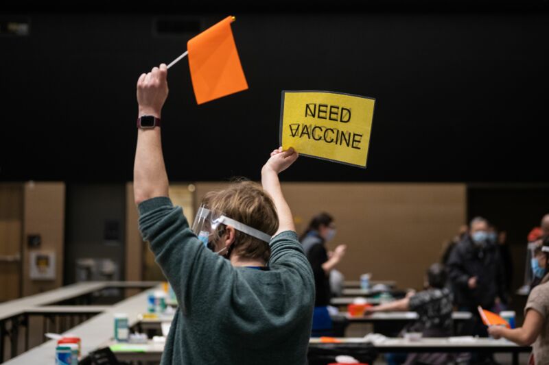 A registered nurse practitioner holds up a sign and a flag asking for another patient to dose with the Pfizer COVID-19 vaccine as well as a more vaccine doses at a vaccination site in Seattle, Washington on January 24, 2021.