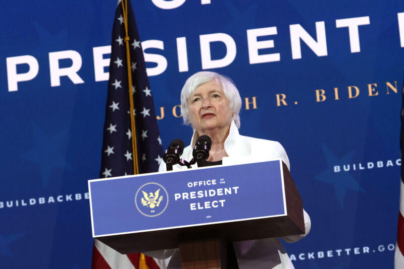 A woman in a white suit speaks at a podium.