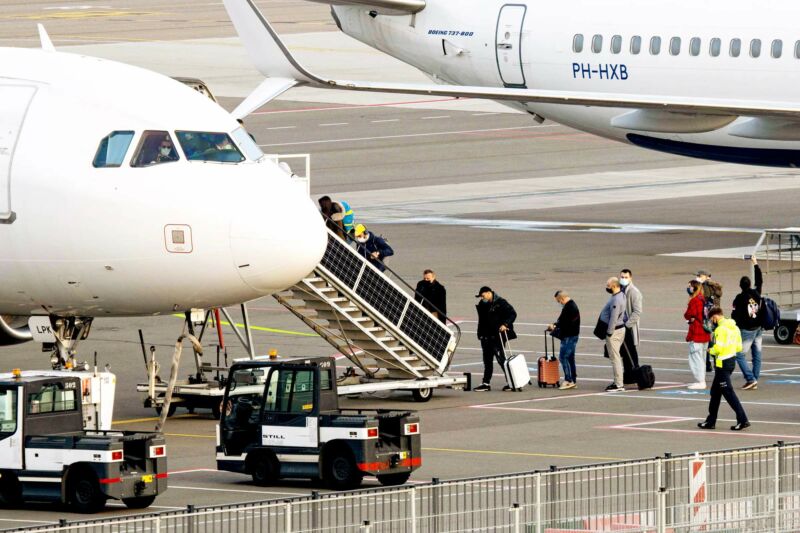Masked passengers board a passenger jet from a runway.