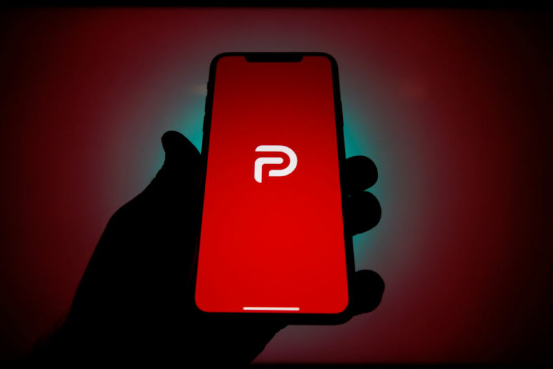 A shadowy hand holds a smartphone displaying the Parler logo.