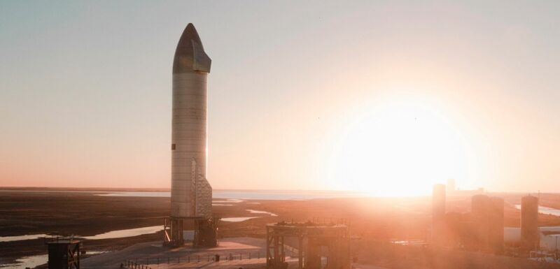 A rocket sits on a launchpad as the Sun blazes on the horizon.