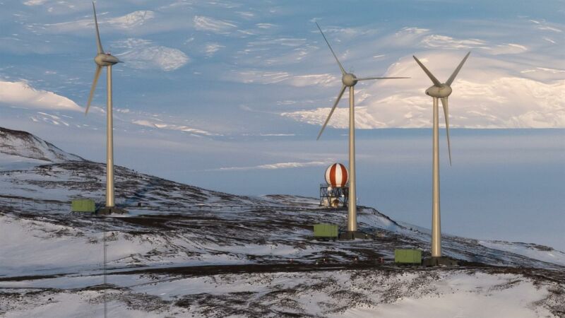 Wind turbines stand above snowy ground.