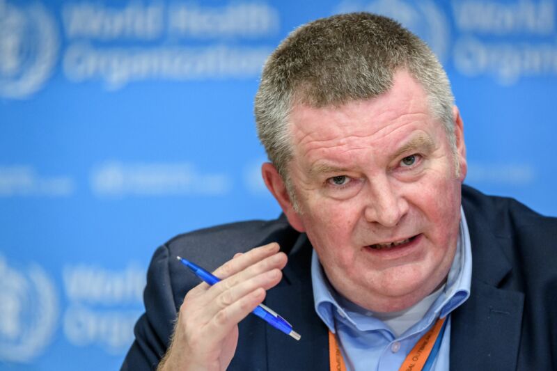 A frustrated man speaks in front of World Health Organization logo.