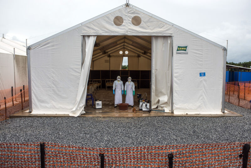 Healthcare workers wearing personal protective equipment stand in a tent with patient beds at an Ebola Treatment Center in Coyah, Guinea, on Thursday, Sept. 10, 2015. 