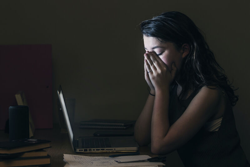 زن جوان ناراحت به جای اینکه به صفحه لپ تاپ خود نگاه کند ، چشمان خود را می بندد.
