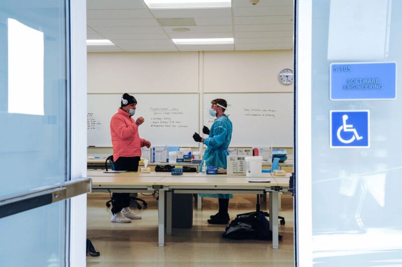 Masked people converse in front of whiteboard.