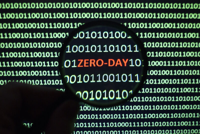 The phrase Zero Day can be seen on a monochrome computer screen clogged with ones and zeros.