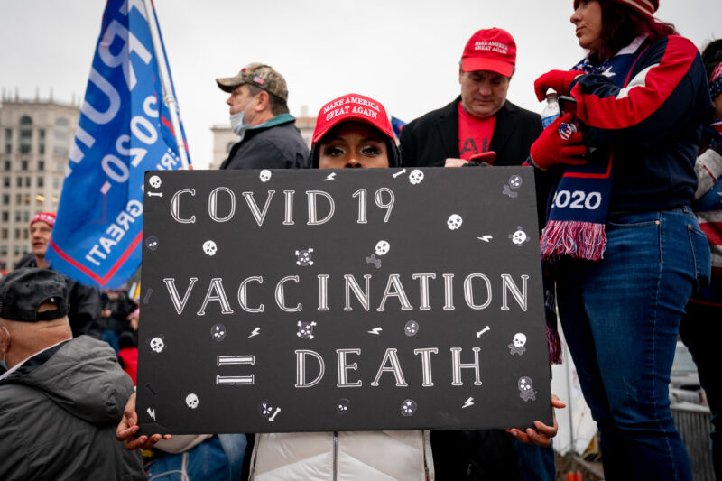 A woman in a MAGA hat holds up a sign reading COVID 19 vaccination equals death.