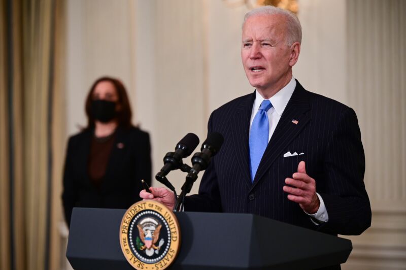 An older man in a suit speaks at a podium with a presidential seal.