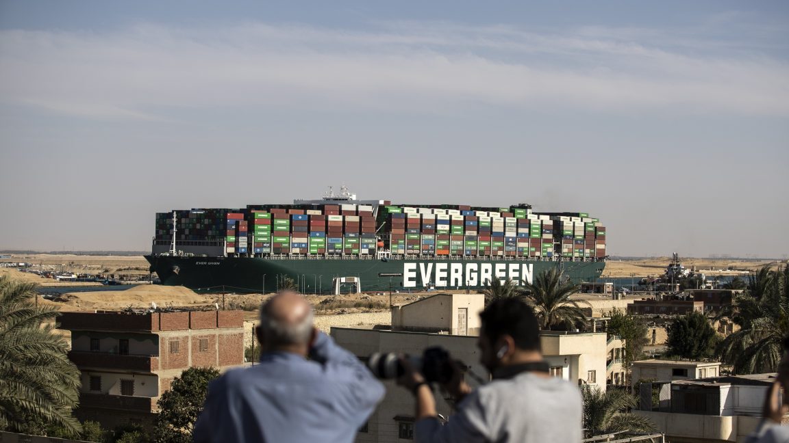 In the foreground, people watch the massive Ever Given ship move from where it was blocking the Suez Canal