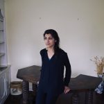 A young woman poses for a photo in a spartan apartment.