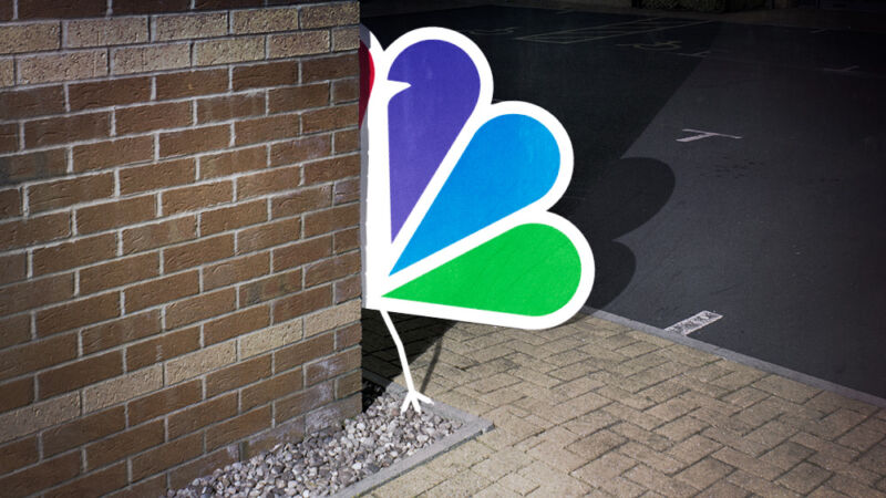 Un logotipo de pavo real de NBC anda suelto y se esconde detrás de la esquina de un edificio de ladrillo.