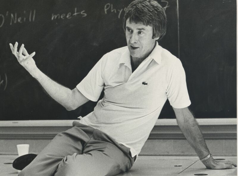 Black and white photograph of a teacher giving a lecture, leaning casually over his desk.