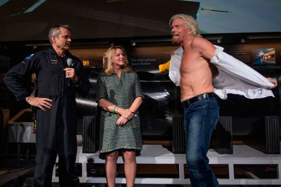 Sir Richard Branson takes off his shirt to don a T-shirt that says "Future Astronaut Training Program." The shirt was given to him by Virgin Galactic Test Pilot Mark "Forger" Stucky as Air and Space Museum Director Ellen Stofan looks on.