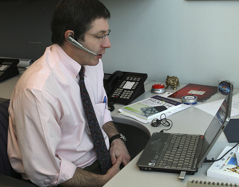 Un hombre con las mangas arremangadas habla con un auricular y mira fijamente una computadora portátil.