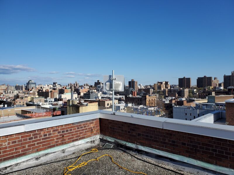 An antenna on a rooftop in the Bronx, with a view of the city during daytime.