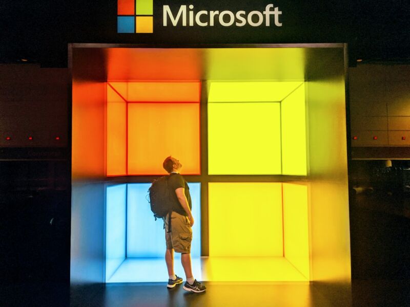 A casually dressed man stands within a giant Microsoft Logo.