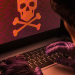 Gloved hands manipulate a laptop with a skull and crossbones on the display.