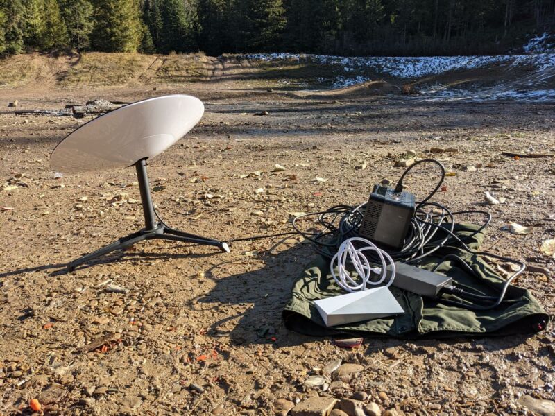 Una antena parabólica Starlink se encuentra en el suelo en un claro en medio de un bosque.