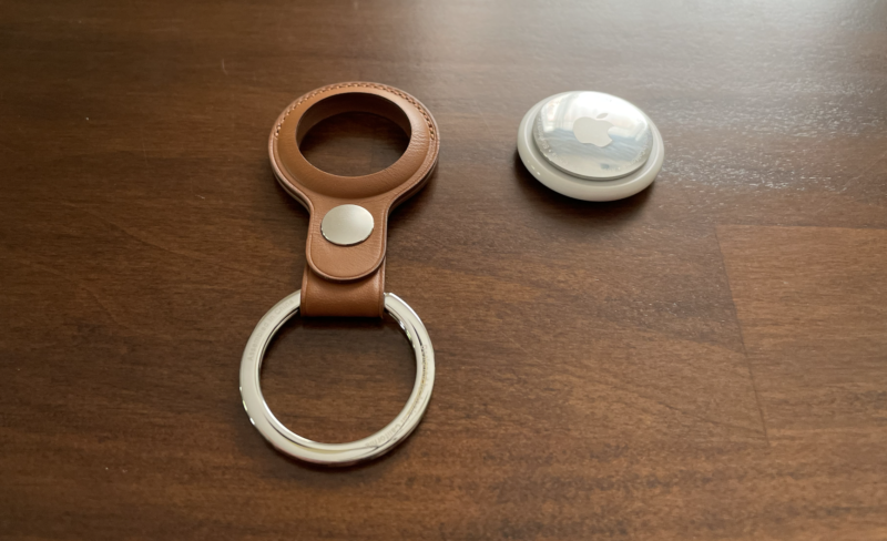 An AirTag next to a keychain with a leather AirTag holder