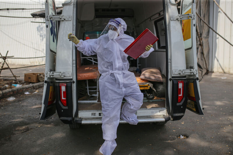 A person wrapped in white protective gear steps out of the back of a van.