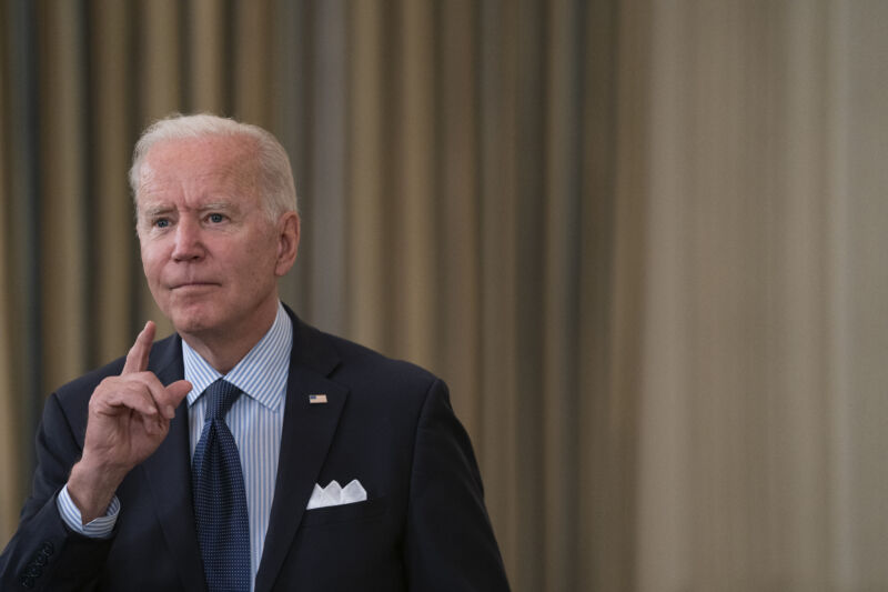 An Older Man In A Suit Gestures While Addressing An Unseen Crowd.