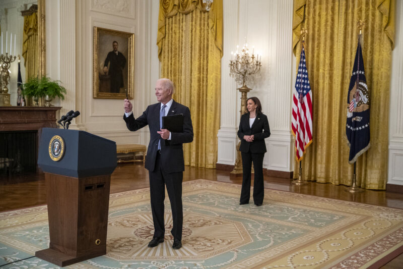 An older man in a suit speaks casually from behind a podium.